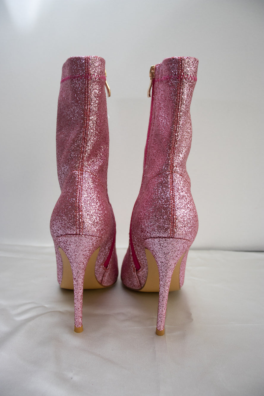 Glitter pink ankle boots shown from the back, highlighting the shimmering finish, zipper detail, and heel shape.