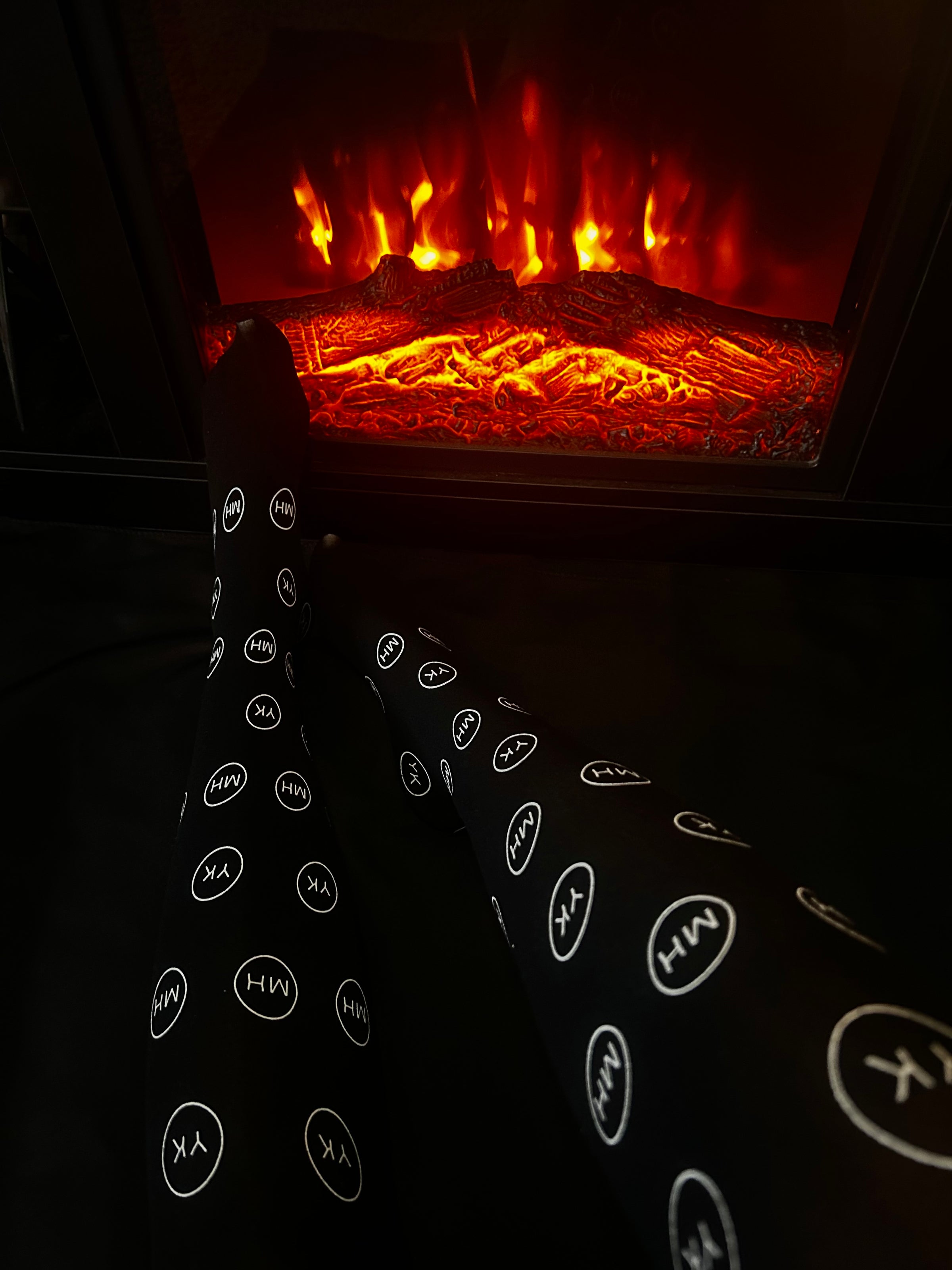 Model wearing black logo over the knee socks by the fire place 